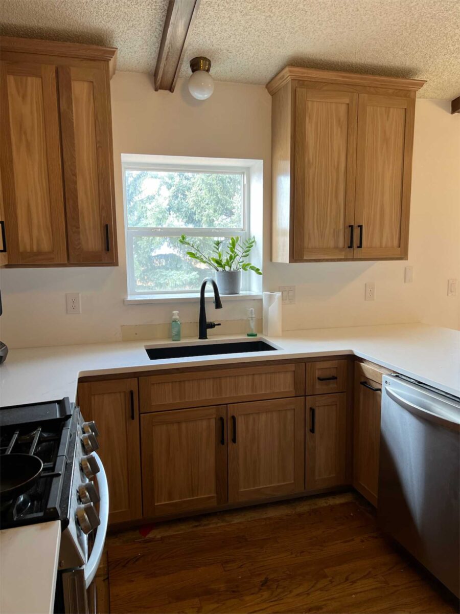 Easy care white countertop complements deep sink area with modern faucet. Window by sinks is flanked by custom built white oak cabinetry with general finish to reveal the natural beauty of white oak wood